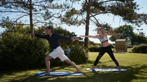 Mann und Frau praktizieren Yoga auf einer Wiese.