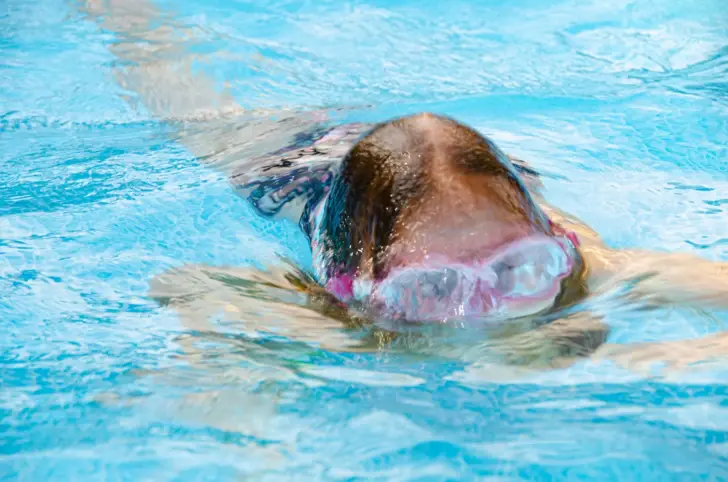 Ein Mädchen mit pinker Schwimmbrille taucht in einem blauen Pool. 