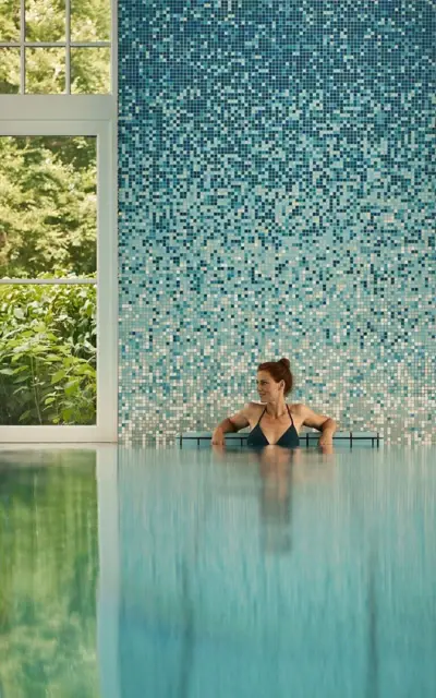 Woman swimming in a pool, surrounded by water reflections.