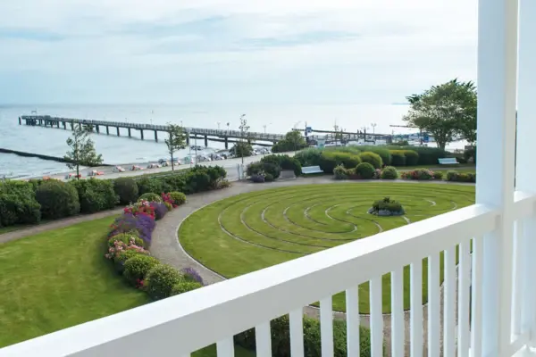 Blick von einem Balkon auf einen Garten und das Meer mit einem Steg.