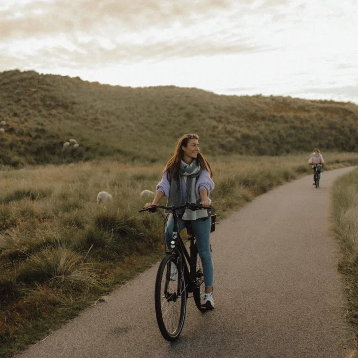 Donna che pedala su un sentiero circondato da erba e colline.