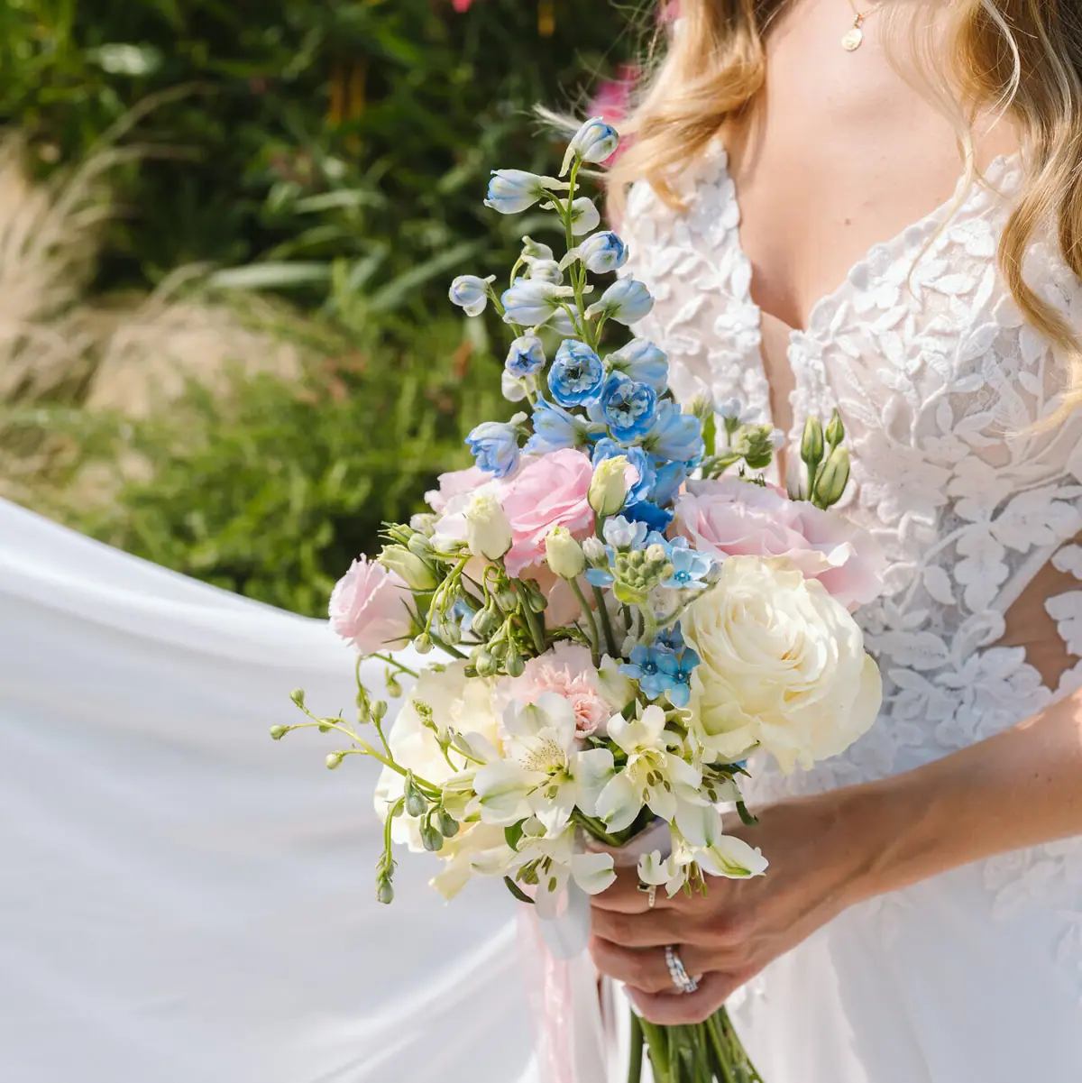 Eine Frau in einem weißen Brautkleid hält einen Blumenstrauß bei einer Hochzeit am Tegernsee.