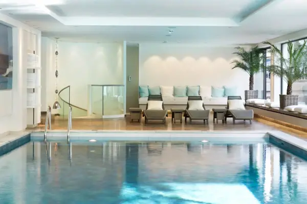 A large indoor pool with a few loungers at the poolside.