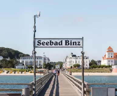 Ein großes Schild mit der Aufschrift Seebad Binz steht vor dem Eingang zu einer Seebrücke.