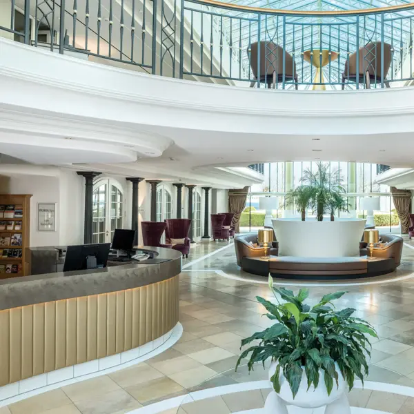 A lobby view of the Kurhaus Binz with the bar, lots of seating and plants. 