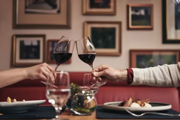 Zwei Personen stoßen mit Weingläsern in einem Restaurant an.