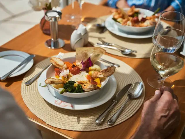 In einer Metallpfanne befindet sich mit Puderzucker überstreuter Kaiserschmarren und Beeren. In der Mitte steht eine kleine Schale mit roter Sauce.