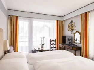 Ein Hotelzimmer mit einem großen Bett, einem alten Holzschreibtisch und orangenen Gardinen.