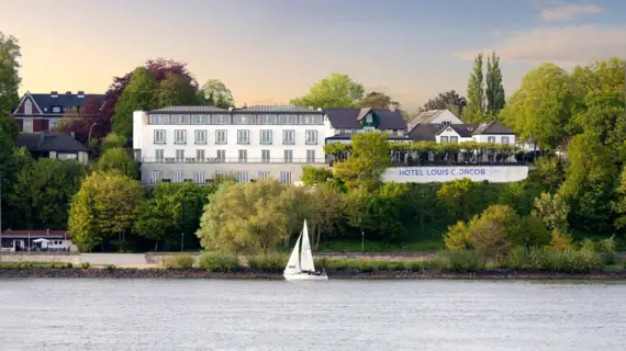 Das Hotel Louis C. Jacob und im Vordergrund befindet sich ein Segelboot auf der Elbe.