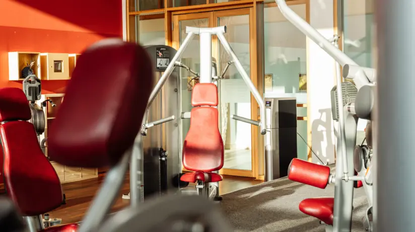 Ein Fitnessbereich mit roten Wänden und Holzboden stehen Sportgeräten mit roten Polstern. 