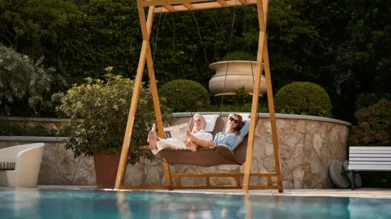  Ein Paar entspannt in einem Hängesessel am Pool.