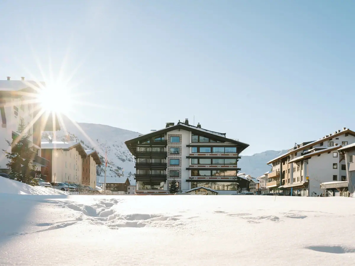 Schneebedeckter Boden mit Gebäuden und Bergen im Hintergrund.
