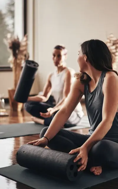 Gruppe von Frauen in Yogakleidung sitzt auf Yogamatten in einem Innenraum.