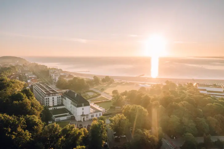 Drohnenaufnahme eines Sonnenaufgangs über dem Strand und A-ROSA Hotel Travemünde.