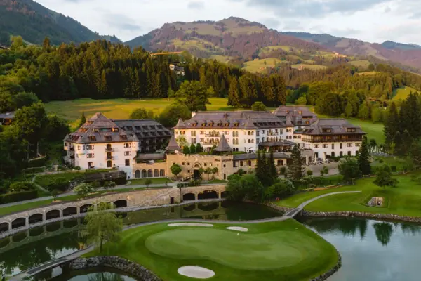 Das Schlosshotel Kitzbühel mit einem Golfplatz und einem See, umgeben von Bäumen und Bergen.