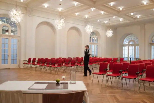 Eine Frau geht in einem großen Tagungsraum mit vielen roten Stühlen.