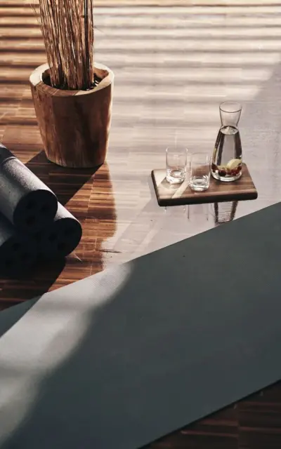 Yoga rolls next to a yoga mat and a wooden tray with two glasses on a wooden floor.