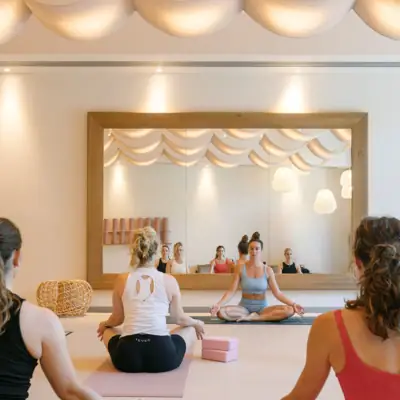 Eine Gruppe von Frauen sitzt in Yoga-Pose in einem Yoga-Raum mit einem Spiegel.