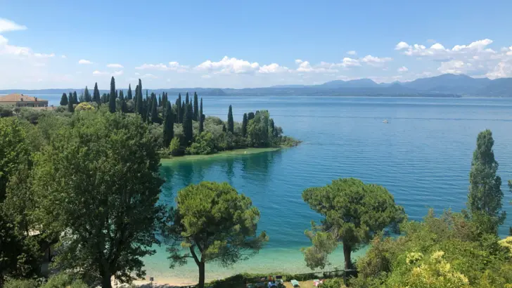 Mediterrane Landschaft mit Bäumen an einem Gewässer unter blauem Himmel.