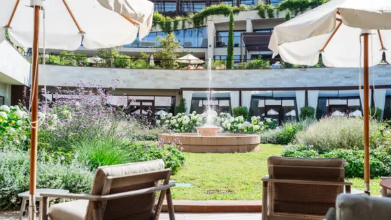 Stühle und Sonnenschirme vor einem Springbrunnen auf einer Terrasse.