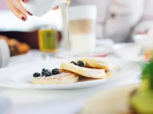 Eine Person gießt Sirup auf Pfannkuchen.