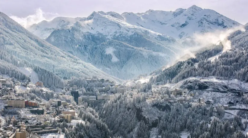 Schneebedeckte Berglandschaft mit einem Dorf im Tal und vielen schneebedeckten Bäumen.