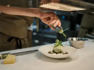 Ein Koch gießt grüne Dressing auf einen Teller mit Essen.