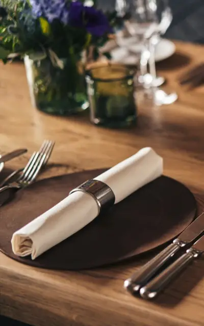 Elegantly laid table with wine glasses and cutlery and a floral decoration in the background.