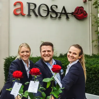 Gruppe von Personen in Anzügen und mit roten Rosen in der Hand lächelt im Freien.