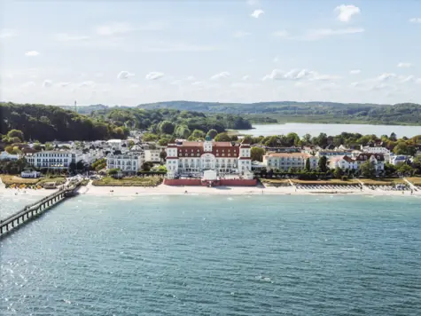 Großes weißes Gebäude an der Küste mit Strand und Meer im Vordergrund.