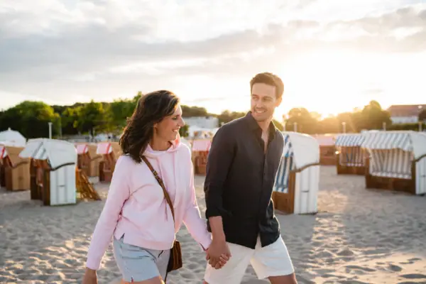 Ein Mann und eine Frau halten sich an einem Strand an den Händen.