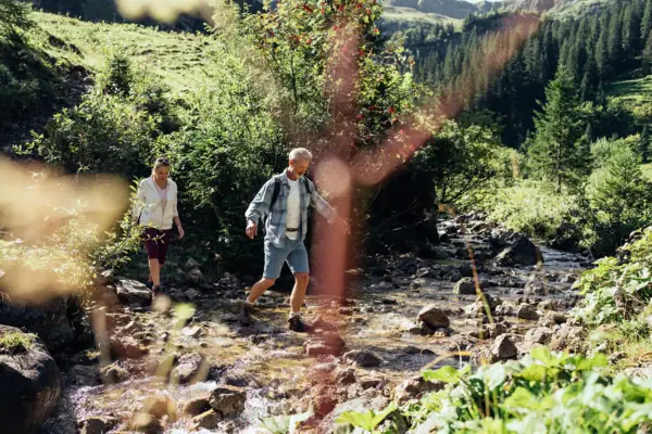 Ein Mann und eine Frau balancieren über Steine in einem Bach.