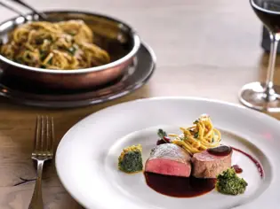 Plate of food on a wooden table, garnished with leafy vegetables.