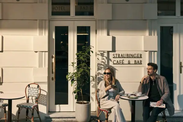 Ein paar sitzt an einem Tisch vor einem Café, isst Kuchen und schaut in die Ferne.