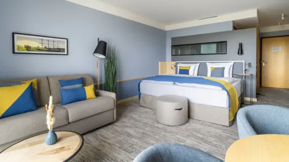 Ein Hotelzimmer mit einem großen Bett, einem grauen Sofa und zwei Sesseln.