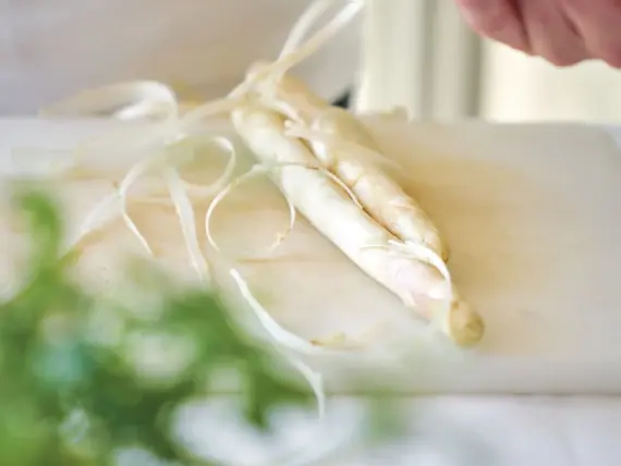 Person schneidet ein Stück weißen Spargel.