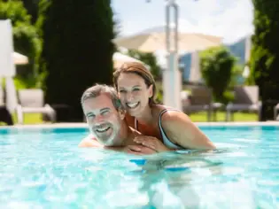 Ein Mann und eine Frau im Freibad, umgeben von Bäumen.