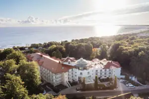 Großes Gebäude mit Bäumen und einem Gewässer im Vordergrund.