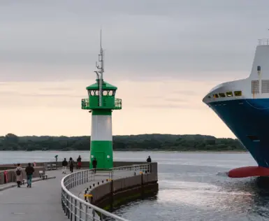 Ein Pier mit einem grün-weißen Leuchtturm neben einem großen Schiff.
