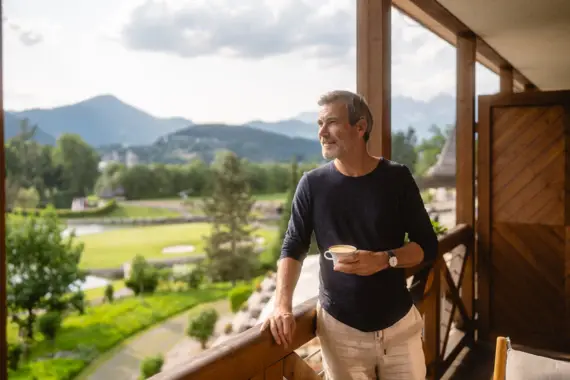 Mann steht auf einer Veranda und hält eine Tasse Kaffee.