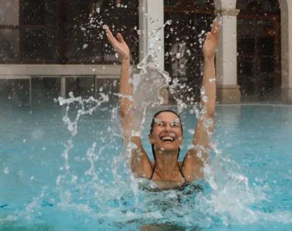 Eine Frau schwimmt glücklich in einem Außenbecken und wirbelt das Wasser durch die Luft. 