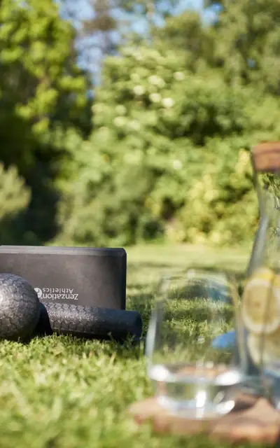 Yogamatten und ein Glas Wasser auf Gras mit grünen Bäumen im Hintergrund.