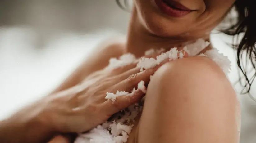 Eine Frau reibt mit ihren Händen ein weißes Peeling über ihre Schulter. 