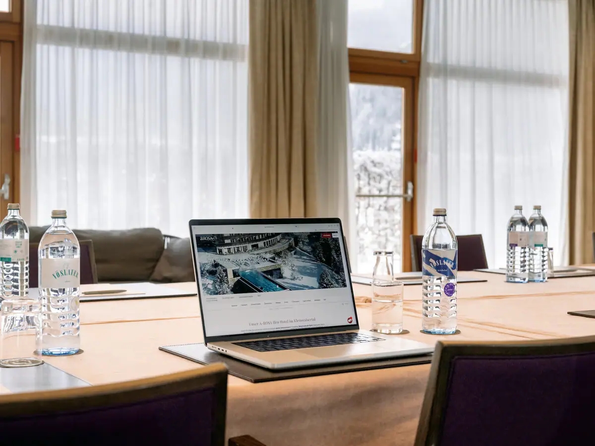 Ein Laptop auf einem Tisch mit Wasserflaschen und einem Fenster im Hintergrund.