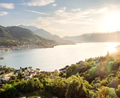 Ein Gewässer umgeben von Bäumen mit Bergen und Gebäuden im Hintergrund.