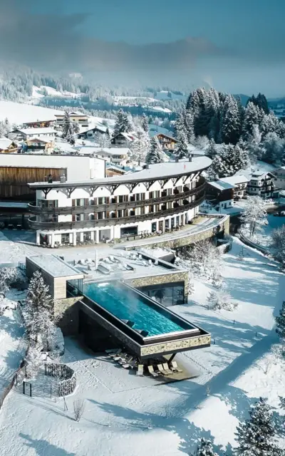 Gebäude mit Infinity-Pool im Schnee, umgeben von Bäumen und winterlicher Landschaft.