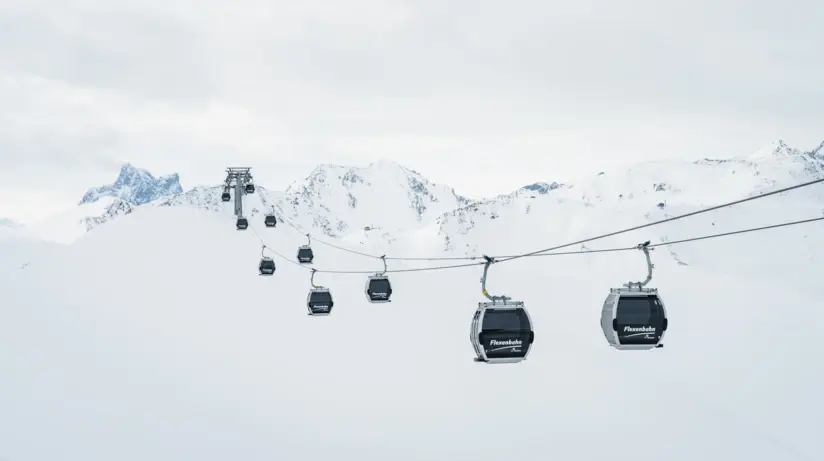 Seilbahn mit mehreren Kabinen über verschneiter Landschaft und Bergen.