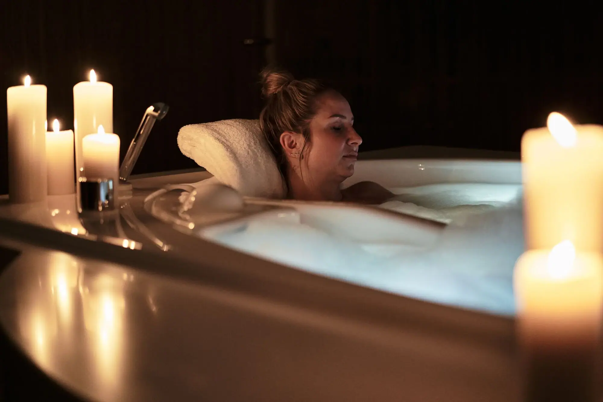 Frau in einem Whirlpool mit Kerzenlicht im Innenbereich.