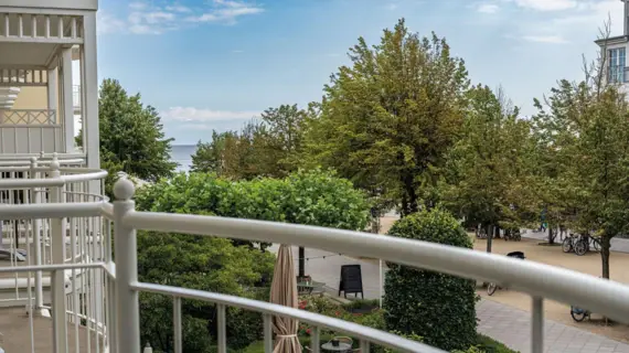 Balkon mit Blick auf eine Promenade mit Bäumen und das Meer im Hintergrund.