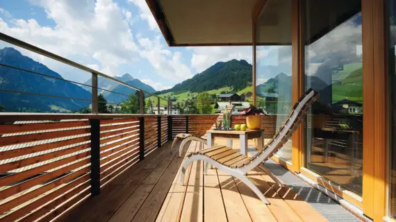 Holzbalkon mit Stühlen und einem Tisch, umgeben von Bergen und Wolken.